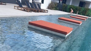 Una piscina con agua azul cristalina, escalones rojos y sillones de descanso.