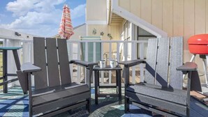 Un área de estar al aire libre con sillas tipo Adirondack y una mesa pequeña, un paraguas a rayas y una parrilla roja.
