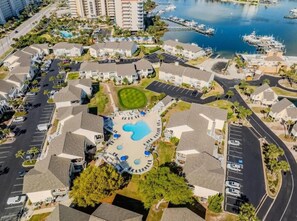 Vista aérea de una zona residencial con piscina central rodeada de casas, un puerto deportivo con barcos y una carretera que serpentea por la propiedad.