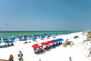 A beach with rows of blue and red umbrellas, white sand, and the ocean in the background. - Emerald Gem *Heated Pool & Private Beach Access* (Destin)