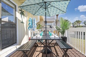 Un patio techado con una mesa y sillas, un paraguas grande y una cerca blanca.