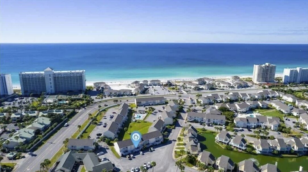 An aerial view of a coastal residential area with multiple buildings, roads, and a beach in the background.