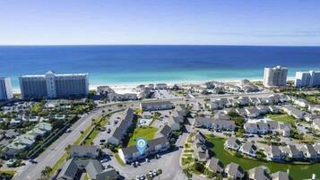 An aerial view of a coastal residential area with multiple buildings, roads, and a beach in the background.