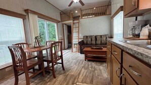 A spacious kitchen with wooden cabinets, a dining area with a table and chairs, and a living area with a sofa. - Campground Tiny Home #46 (Huntsville)