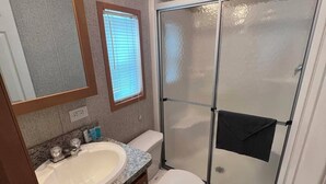 A bathroom with a sink, toilet, and glass shower enclosure. - Campground Tiny Home #46 (Huntsville)