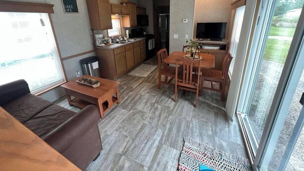 A compact living space with a kitchenette, a dining area, and a seating area with a sofa and table. - Campground Tiny Home #46 (Huntsville)
