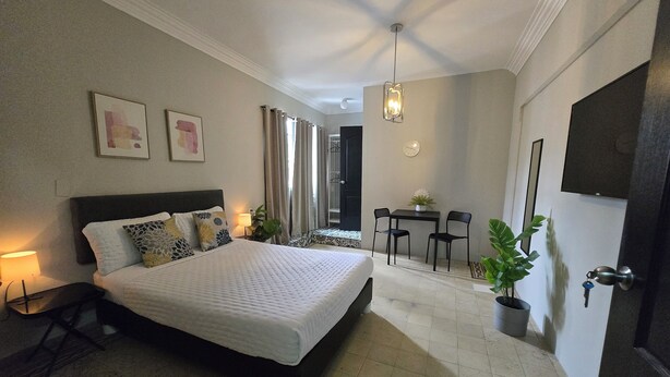 A bedroom with a bed, bedside table, lamp, and a small table with chairs.