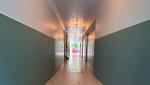 A long, narrow hallway with a tiled floor and walls painted in two-tone colors. There are black mats at the entrance, and a ceiling light fixture with multiple bulbs.