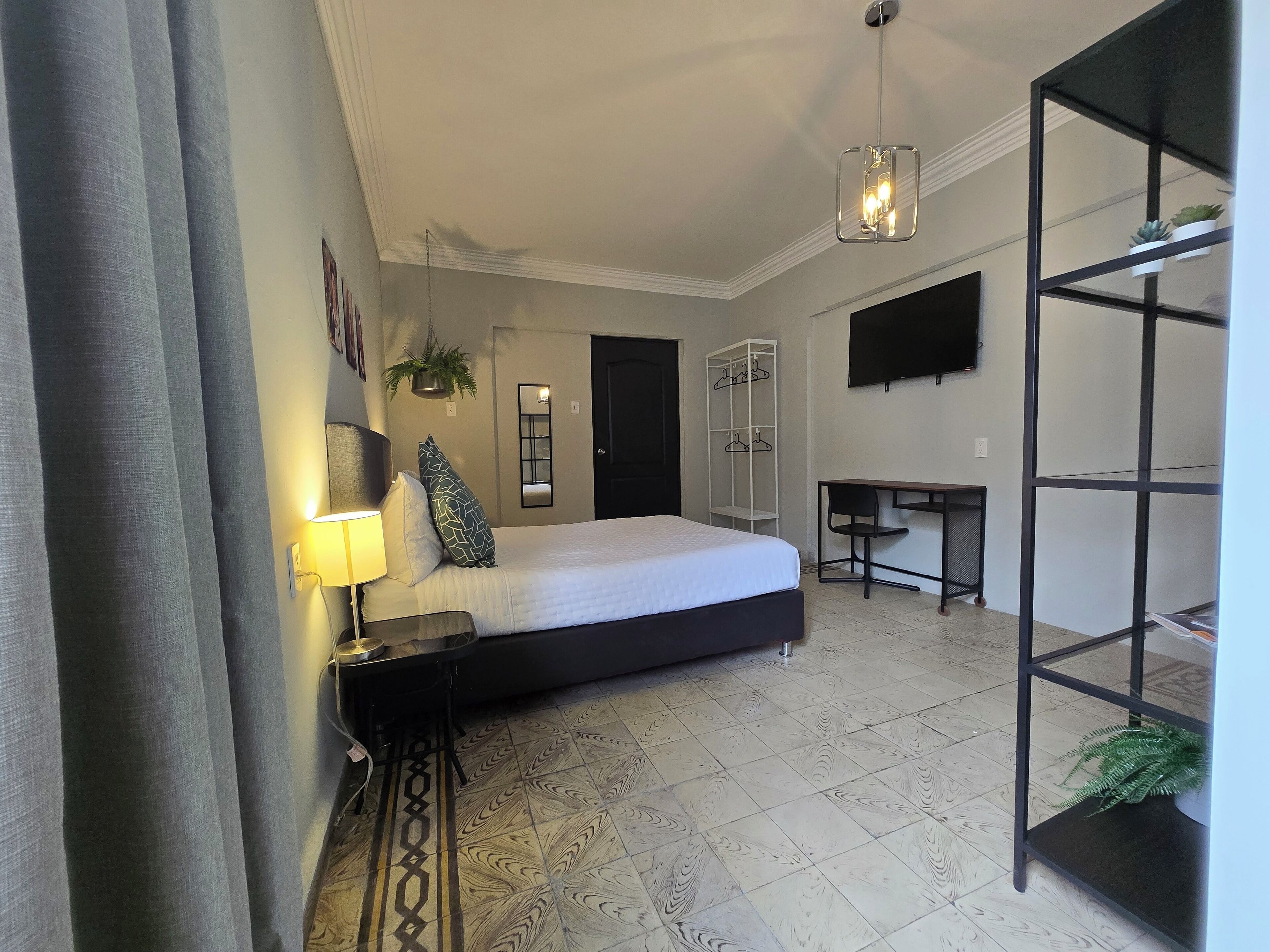 A hotel room with a bed, bedside table, lamp, desk, chair, and a TV mounted on the wall.
