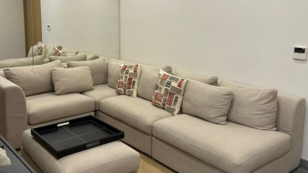 A modern living room with a beige sectional sofa, a small ottoman, and a black tray table. - Business studio-apartment near the beach (Cancún)