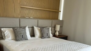 A modern hotel room with a large bed, grey upholstered headboard, and a wooden shelf above. - Business studio-apartment near the beach (Cancún)