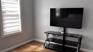 A bedroom with a bed, a TV on a black stand, a window with blinds, and wooden flooring. - "Serene Escape: Leave Worries Behind"
 (Wilkes-Barre)