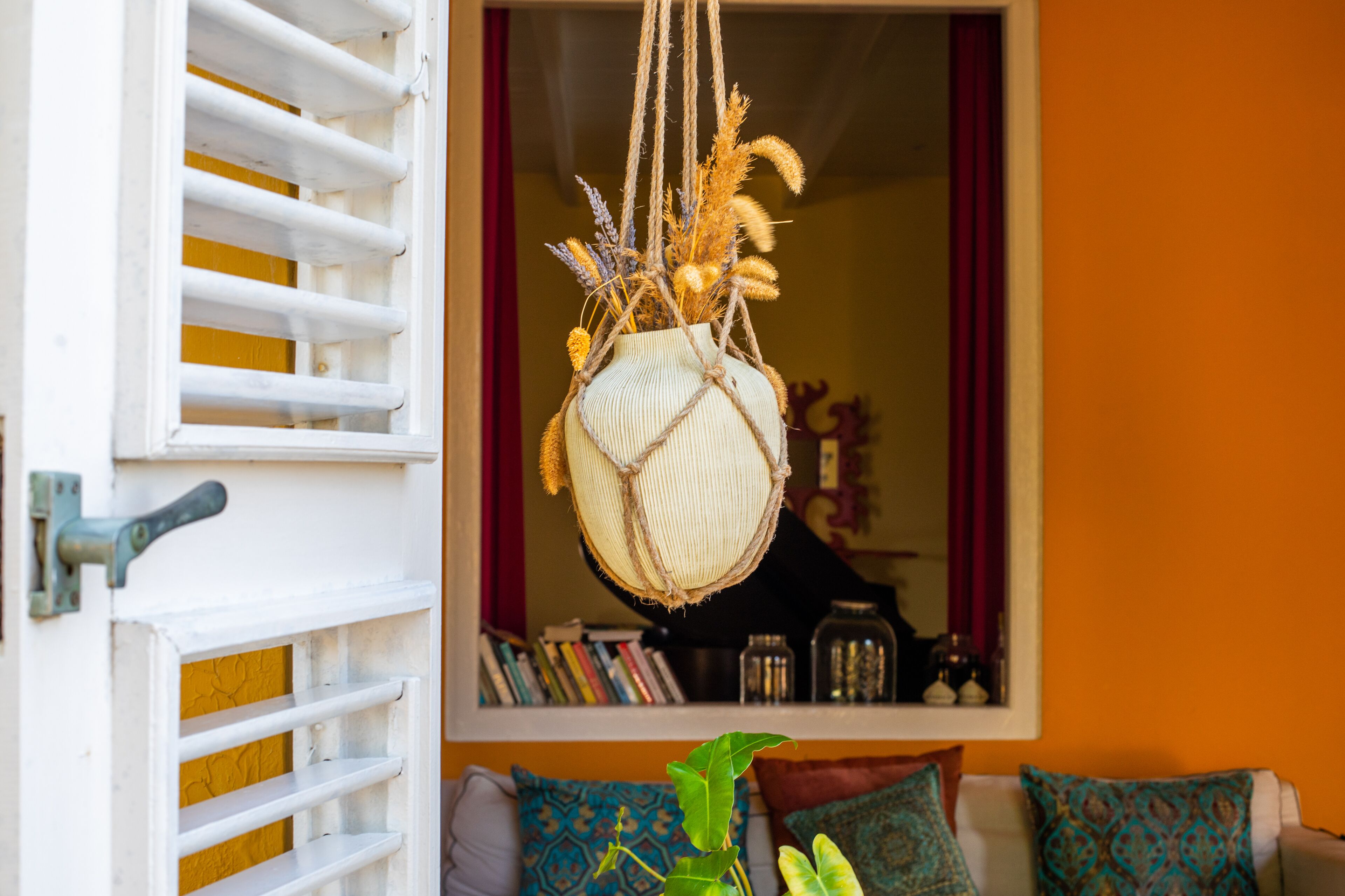 A room with a white door, a hanging plant, a bookshelf, and a sofa with patterned cushions.