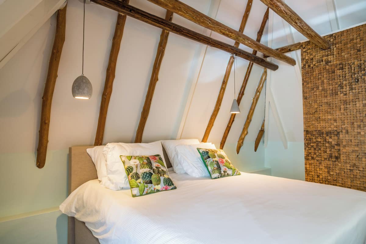 Een bed met twee decoratieve kussens, houten balken, een hanglamp en een structuurwand.