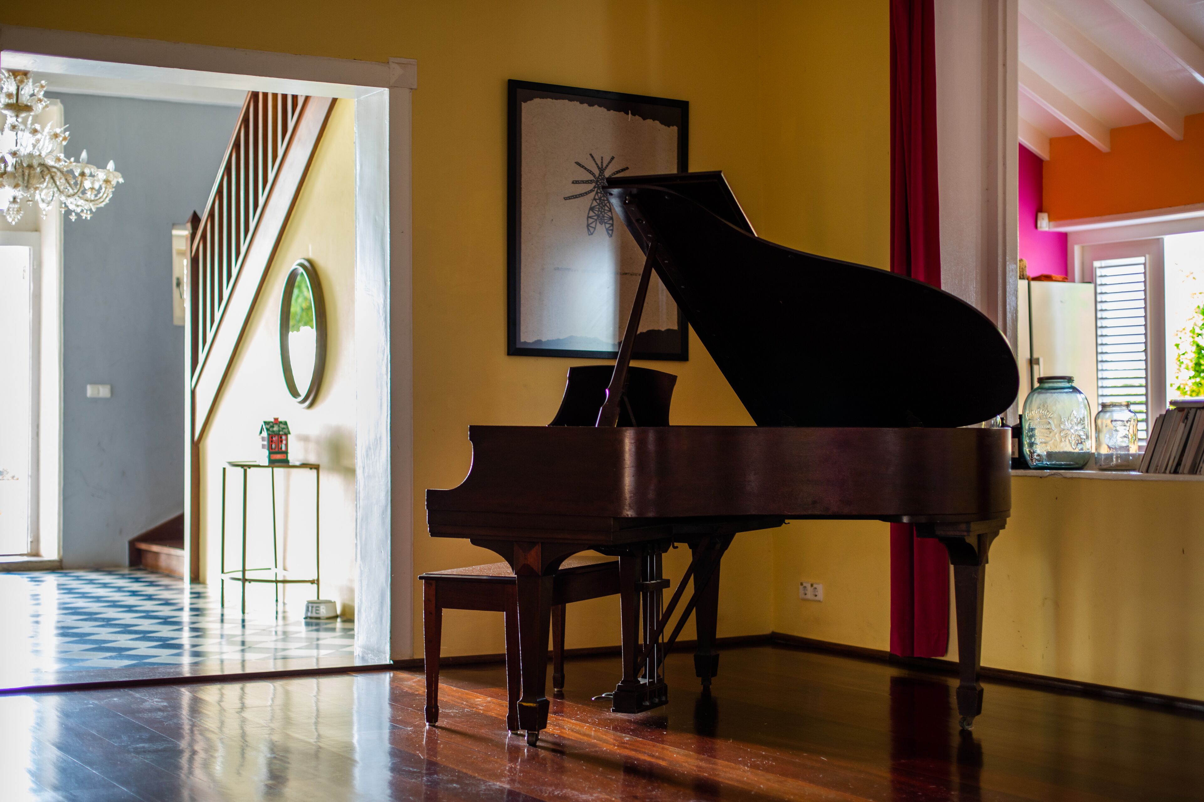 Een vleugelpiano in een ruime kamer met houten vloer, een trap en een kroonluchter.