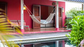 Un edificio rojo con piscina, hamaca y puerta de madera.
