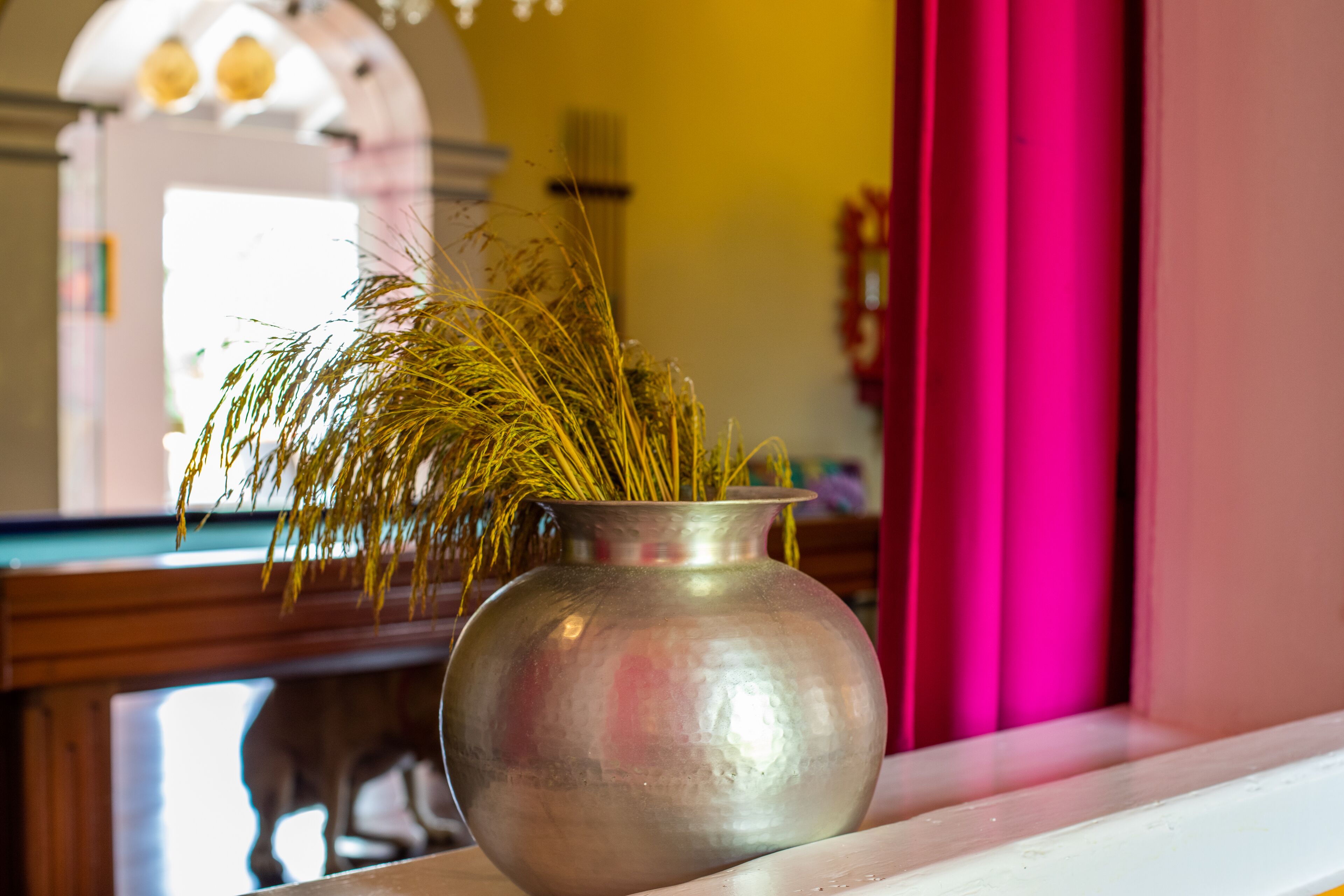 A metallic vase with dried grass on a white surface.