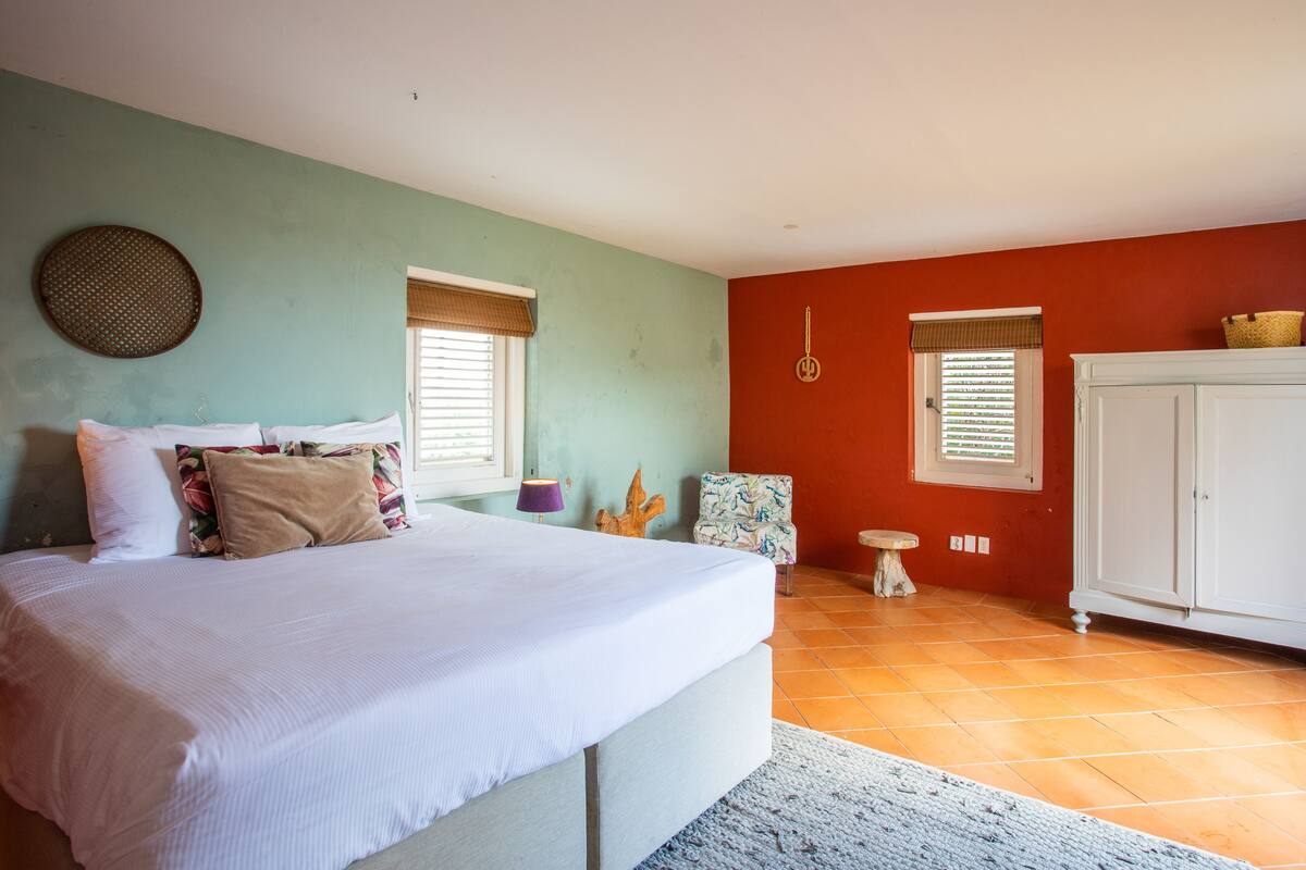 Een slaapkamer met een bed, twee ramen, een stoel, een kast en een vloerkleed.