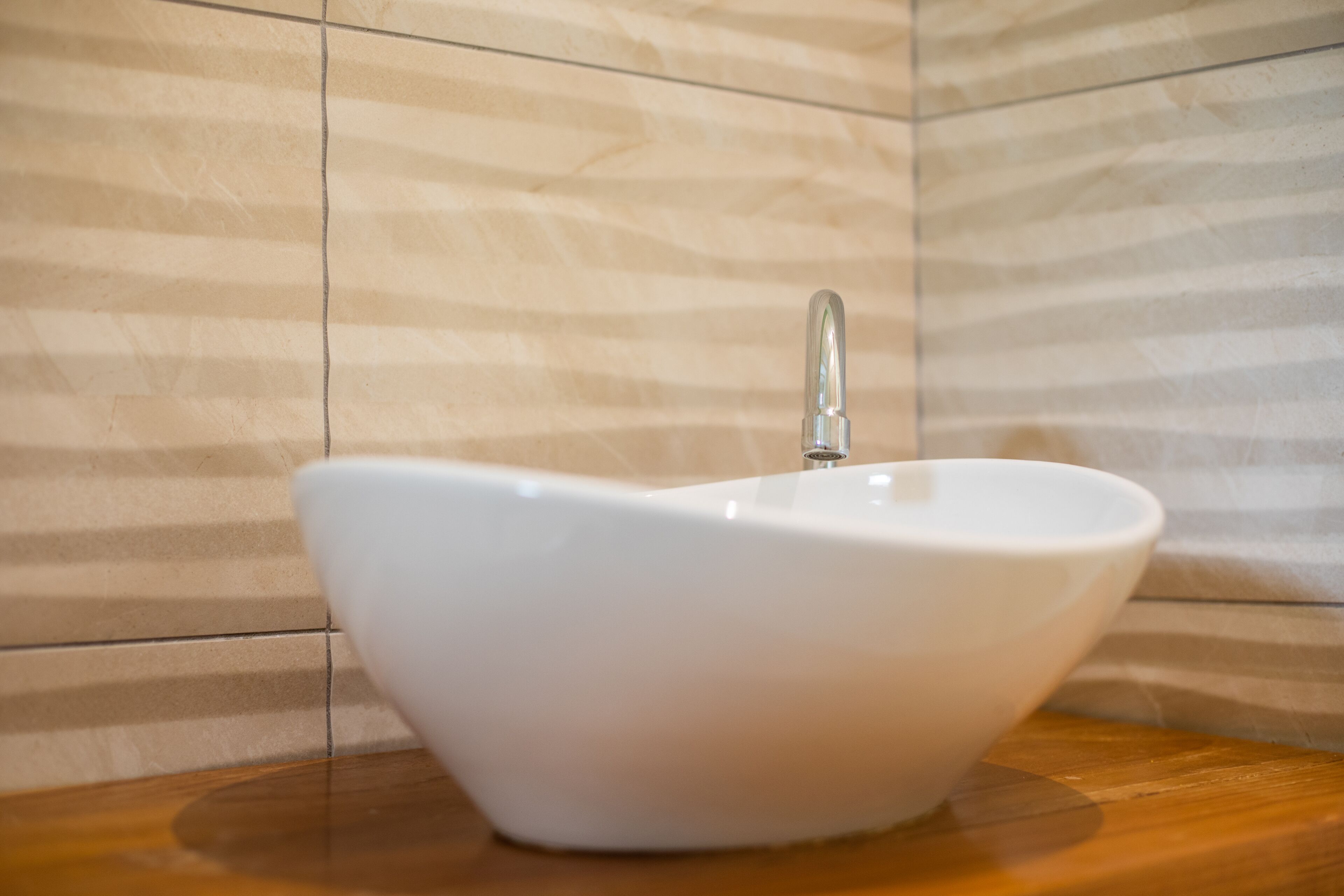 Un lavabo de cerámica blanca con un grifo moderno, frente a una pared beige texturizada, sobre una encimera de madera.