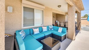 A covered outdoor seating area with a sectional sofa, a glass-top table, and a clock on the wall.