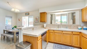 A modern kitchen with wooden cabinets, a built-in dishwasher, a dining area with a bench, and a window with blinds.