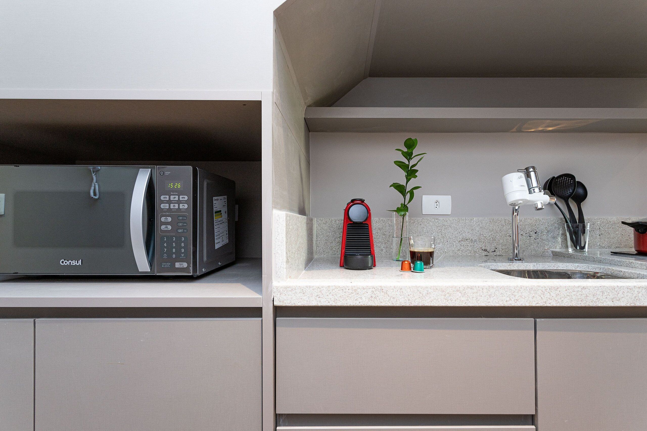 A kitchen with a microwave, a red coffee maker, a plant, and a sink.