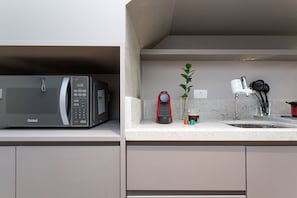 A kitchen with a microwave, a red coffee maker, a plant, and a sink. - Next Haddock by Viva - Apartamentos próximos ao MASP e a metros da Estação Consolação e Avenida Paulista (São Paulo)