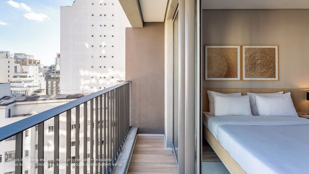Una habitación de hotel con balcón, una cama y dos cuadros enmarcados en la pared.
