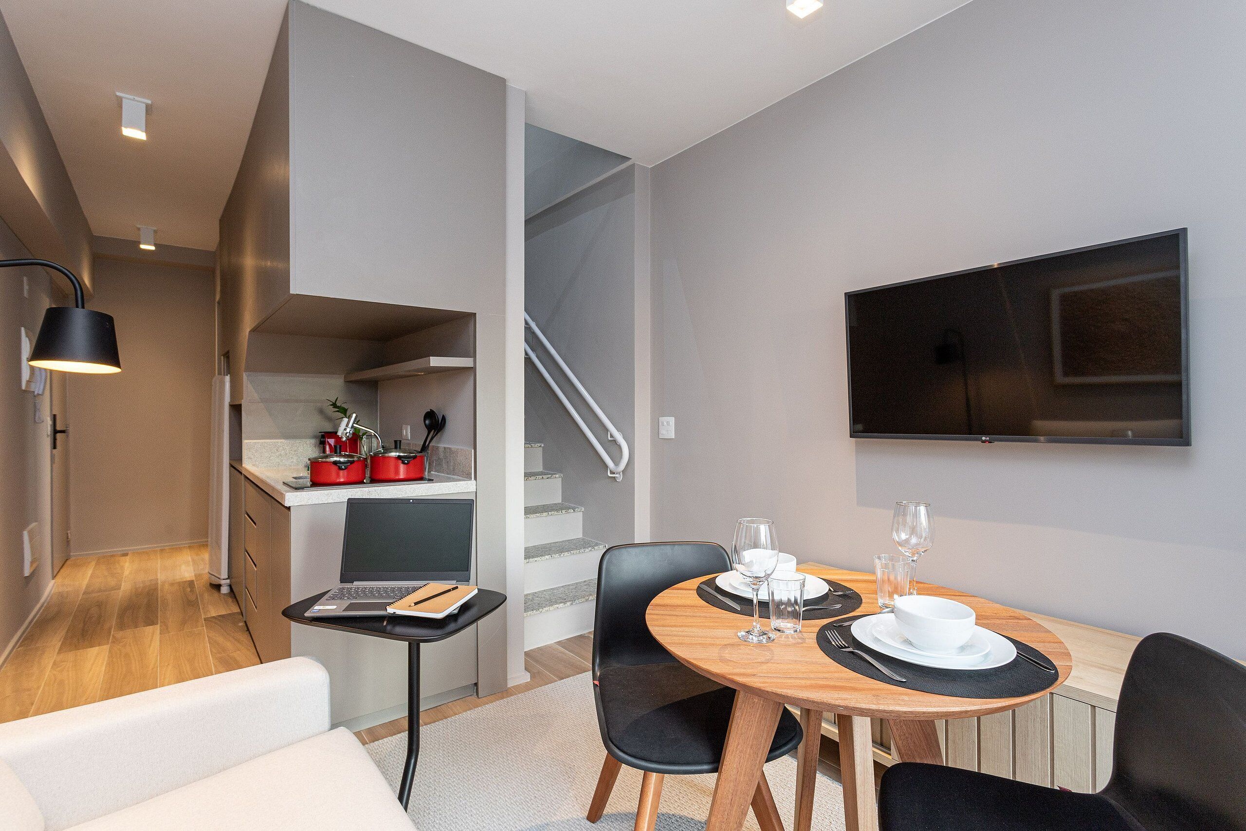 Ein modernes Hotelzimmer mit Essbereich, einer Küche und einem an der Wand befestigten Fernseher.