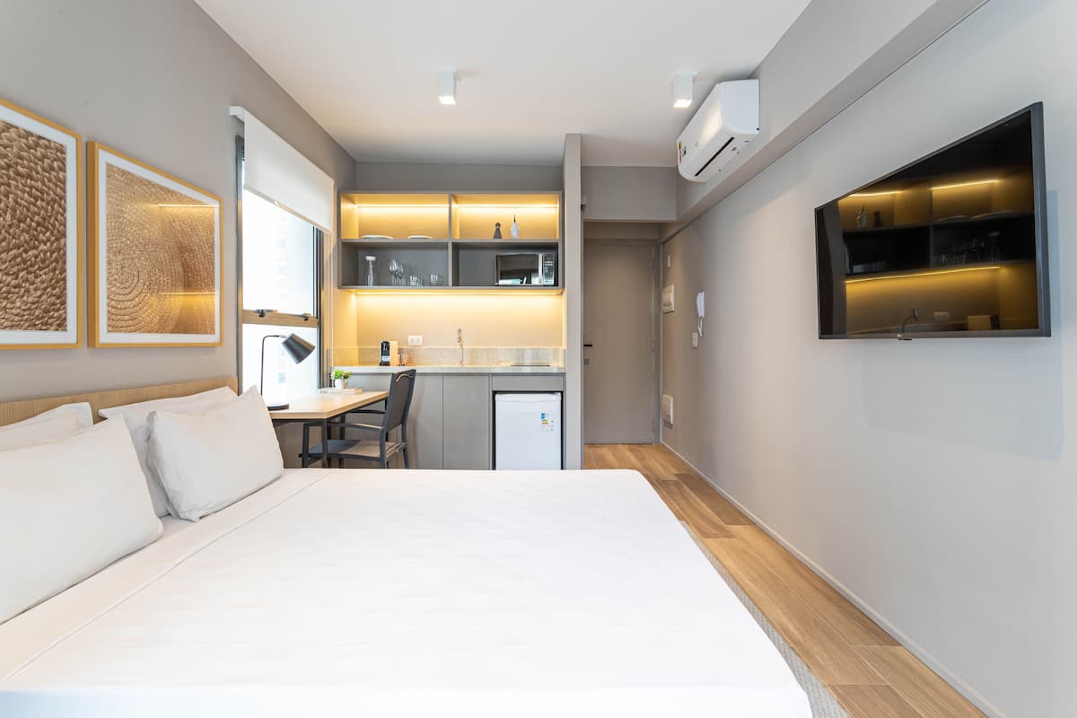 Ein modernes Hotelzimmer mit einem großen Bett, einer kleinen Küchenzeile und einem an der Wand montierten Fernseher.