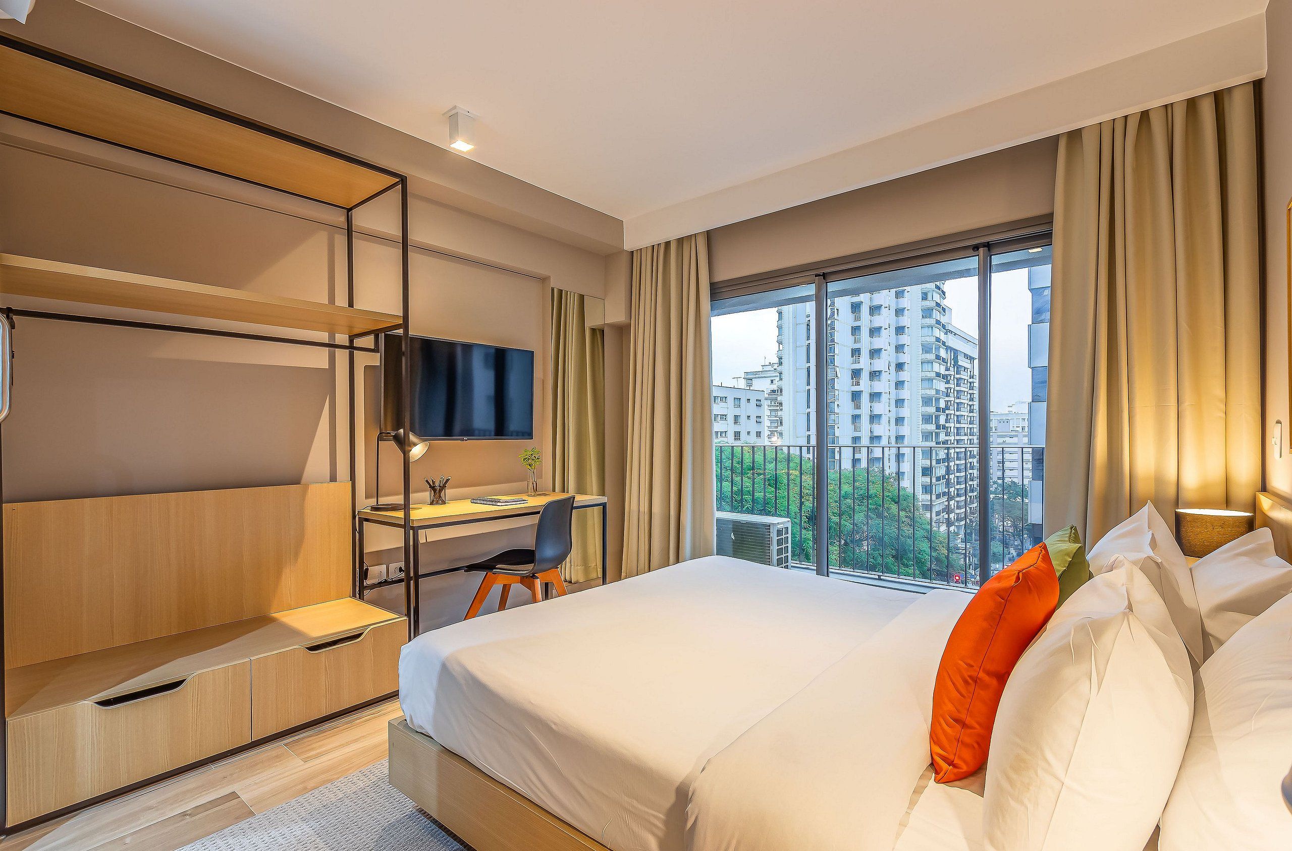 A hotel room with a bed, a desk, a TV, and a view of the cityscape.