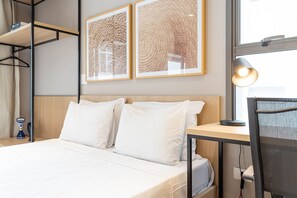 A hotel room with a bed, two pillows, a desk with a lamp, a chair, and two framed artworks on the wall. - Next Haddock by Viva - Apartamentos próximos ao MASP e a metros da Estação Consolação e Avenida Paulista (São Paulo)