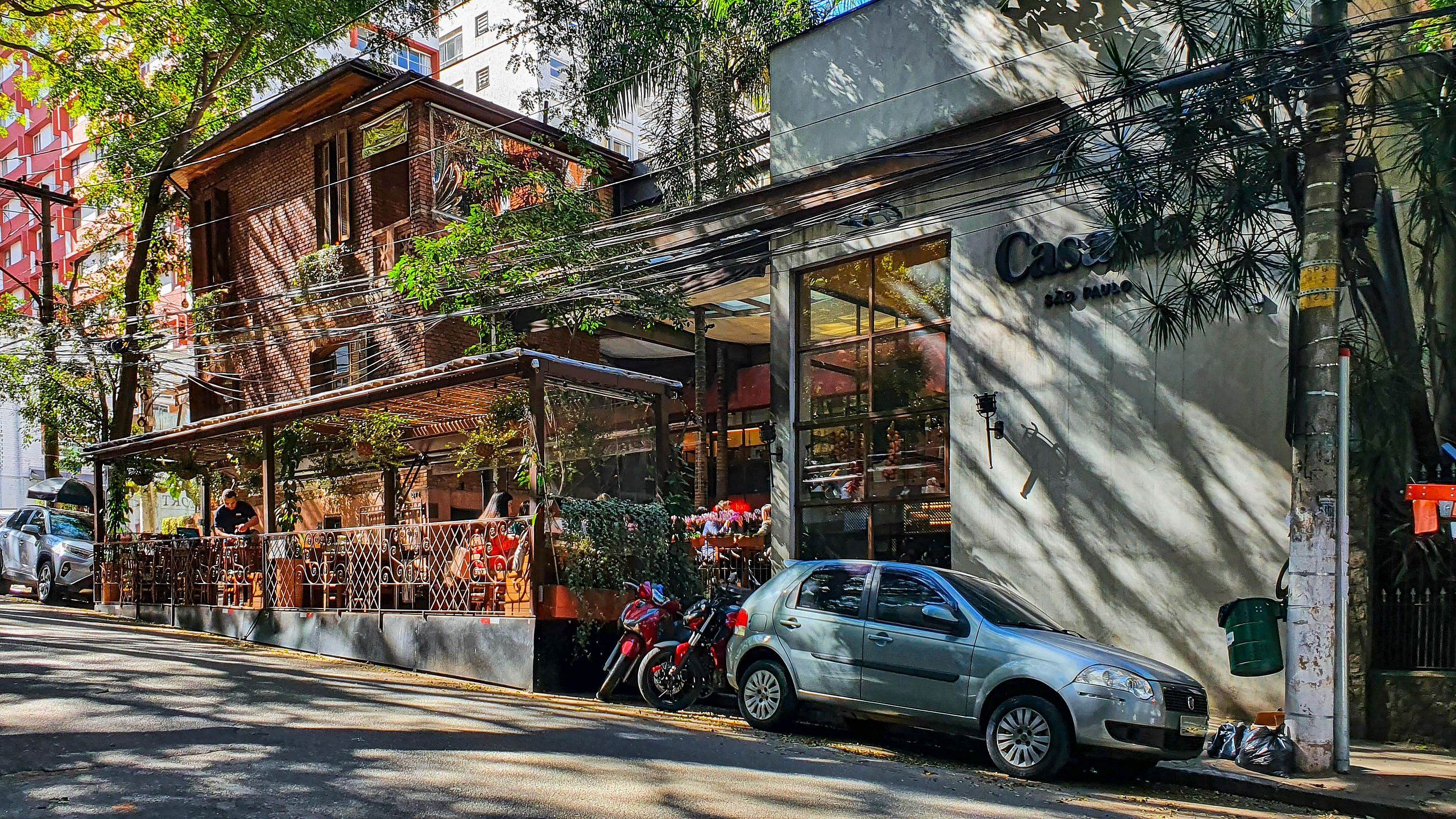 A street view with a building featuring a storefront, a parked car, and a motorcycle.