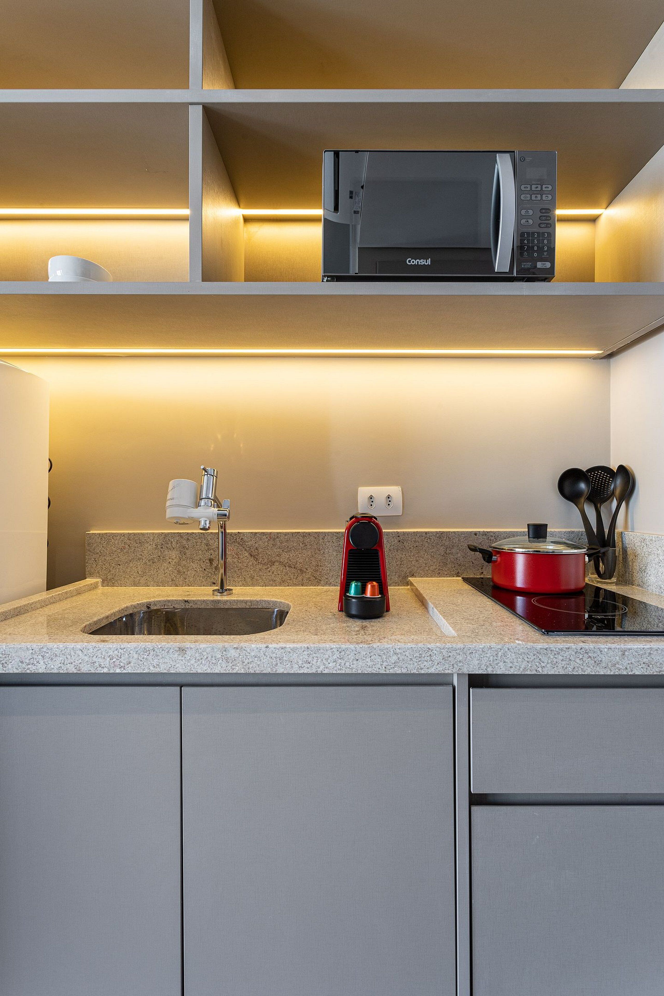 Una cucina moderna con un forno a microonde integrato, una macchina per il caffè e una pentola rossa sul fornello.