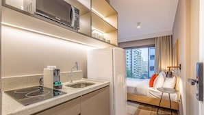 A compact hotel room with a kitchenette, a bed with a view, and a small bedside table. - Next Haddock by Viva - Apartamentos próximos ao MASP e a metros da Estação Consolação e Avenida Paulista (São Paulo)