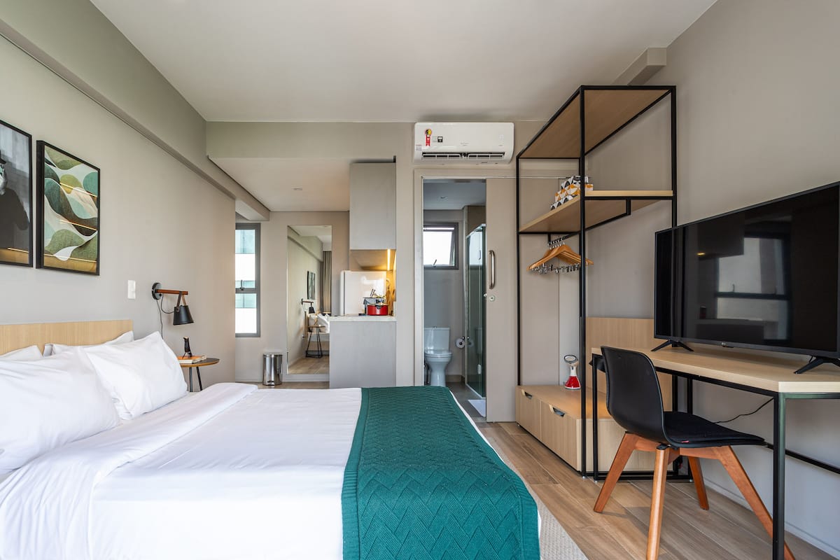Ein Hotelzimmer mit Bett, Schreibtisch mit Stuhl, Fernseher und einem durch eine offene Tür einsehbarer Badezimmer.