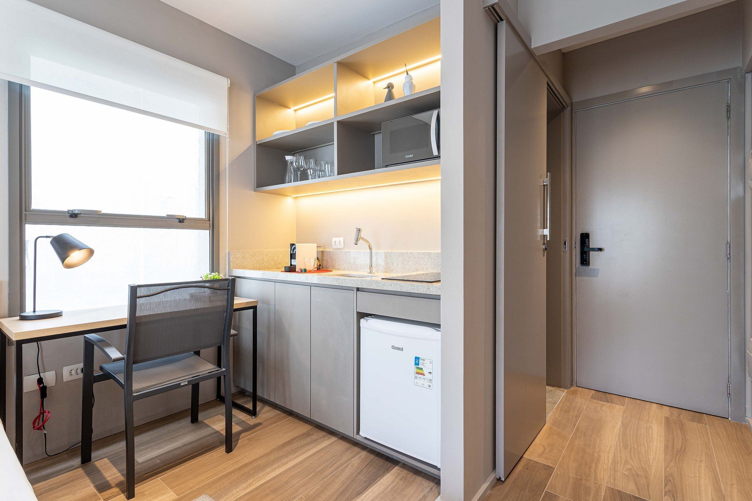 A compact kitchen with a built-in dishwasher, a dining area with a chair, and a window providing natural light.