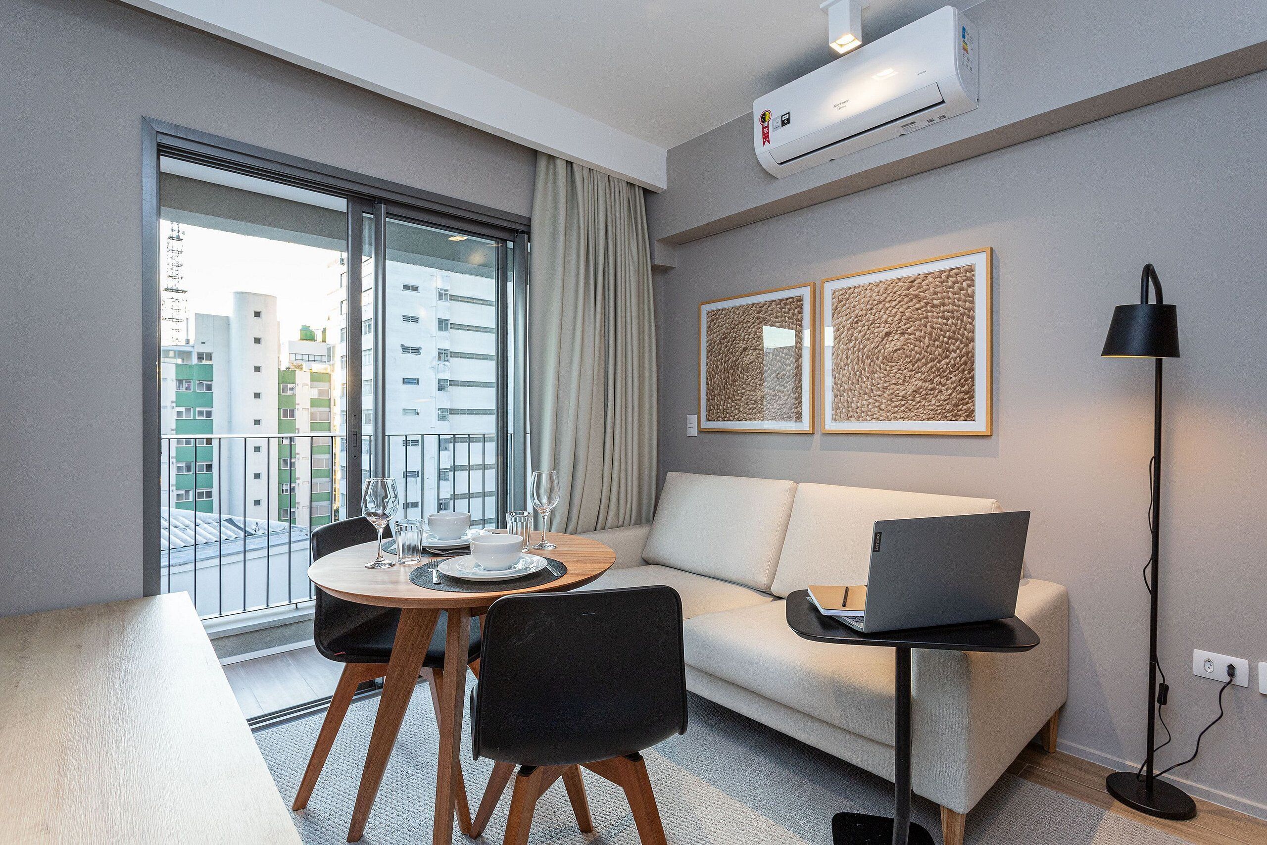 A modern hotel room with a dining area, a sofa, and a laptop on a small table.