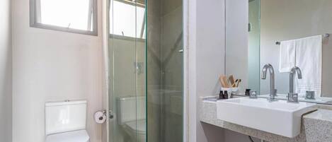 Een badkamer met een douchecabine van glas, een wit toilet en een wastafel met spiegel.
