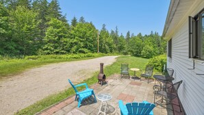 A patio with outdoor furniture, a wood stove, and a view of a forested area. - Charming & Scenic Gouldsboro Getaway w/ Patio! (Gouldsboro)
