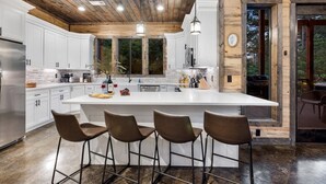 Une cuisine moderne avec des meubles blancs, un grand îlot central doté de tabourets et un plafond en bois.