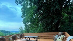 Una terraza de madera con una mesa de picnic y sillas, rodeada de vegetación exuberante y vistas al paisaje.