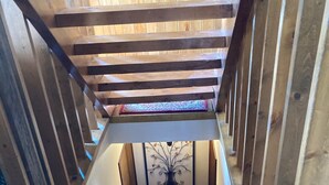 Una escalera de madera con barandilla, que conduce a una plataforma con un tapete estampado y un adorno en la pared.