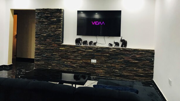 Een moderne woonkamer met een stenen accentmuur, een wandgemonteerde flatscreen-tv en een bank.