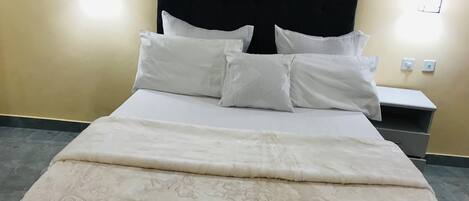 A neatly made bed with a patterned bedspread and white pillows, a dark headboard, and two wall-mounted light fixtures.