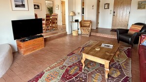 A spacious living room with a television, a wooden coffee table, and a patterned rug. - Vista Gloriosa - panoramic mountain views in Eldorado. (Santa Fe)