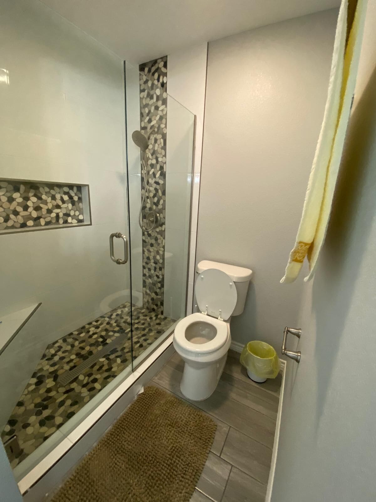 Un baño con ducha de vidrio, inodoro y una alfombra pequeña.