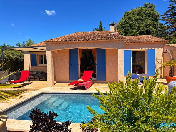 A poolside area with a tiled roof, red lounge chairs, and a small building with blue shutters.