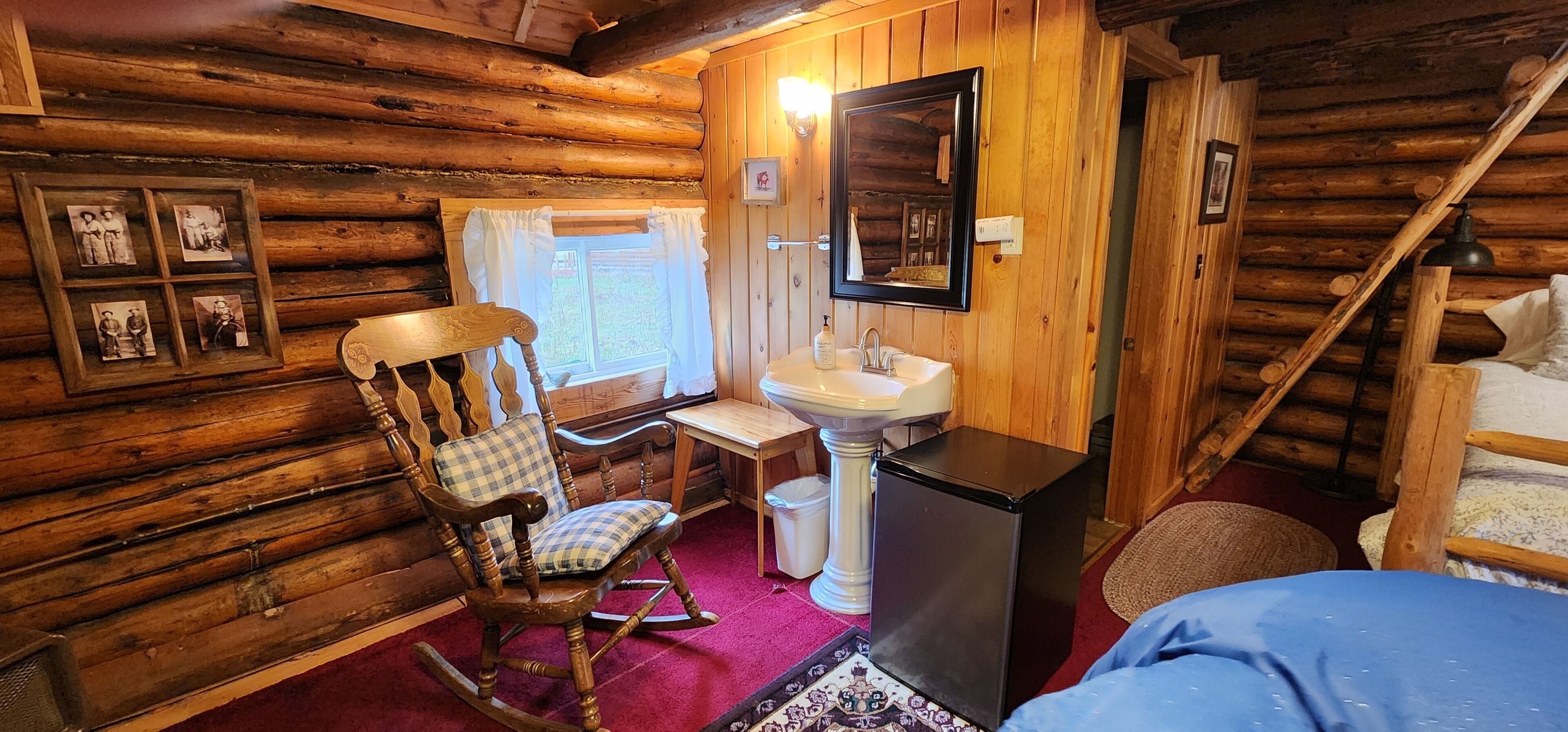 A log cabin room with a rocking chair, a small table, a sink, and a mirror.