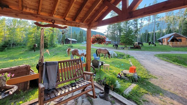A wooden gazebo with a bench and hanging decorations, overlooking a rural landscape with horses and cabins. - Bear Creek Guest Ranch (Essex)